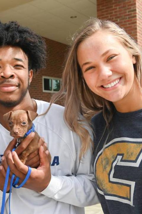 Two students with a tiny puppy