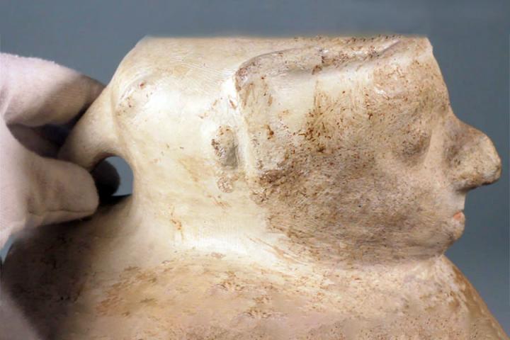 Pre-Columbian ceramic vessel with a human face designed into the neck, containing two eyes, a protruding nose, and a mouth.