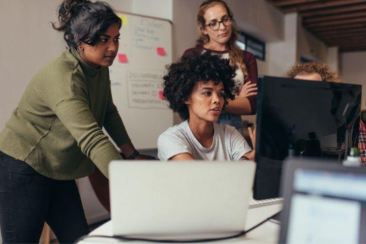 A group of software engineers talking with one another while one sits at a desk