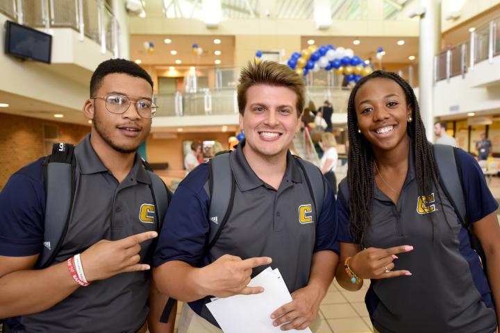 Two male and one female student wearing blue Chattanooga polos holding up the Power C hand gesture during an orientation.