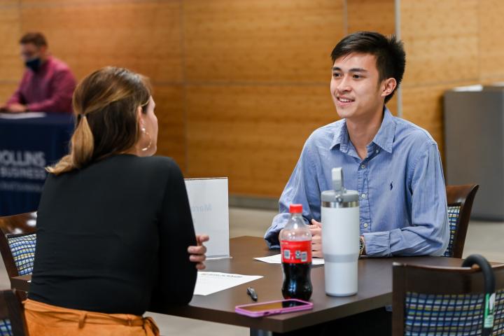 Student in a blue button down shirt talking with a woman in a black jacket.