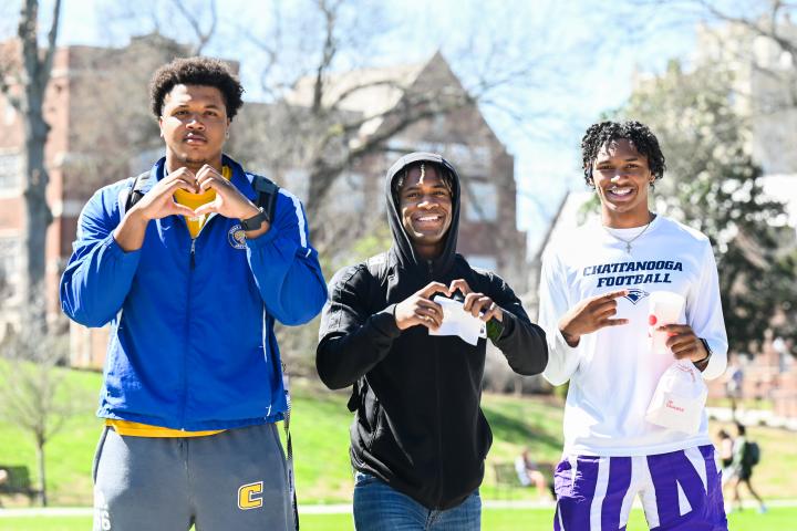 Three male students holding up the Power C and heart hand gestures.