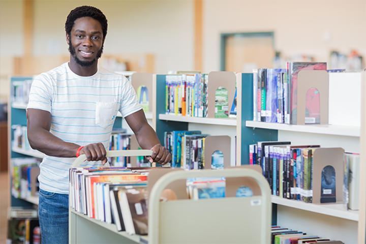 Photo of a student with a cart full of books to be reshelved.