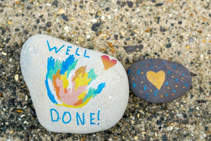 Photograph of two smooth river rocks painted with cheerful slogans and hearts.