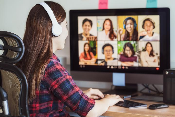 female student in an online class with headphones on and 8 students showing on her computer screen