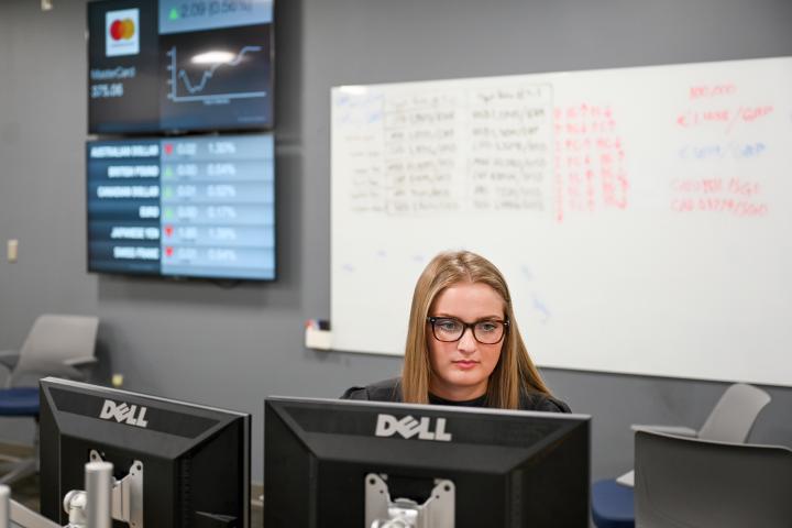 UTC Business Analytics student looking at a computer with stock data on a screen in the background