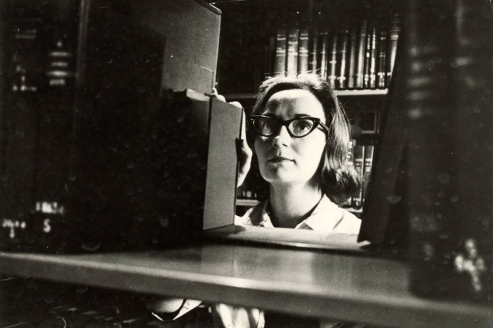 Black-and-white photograph of a student looking at books in the Fletcher Hall library. 