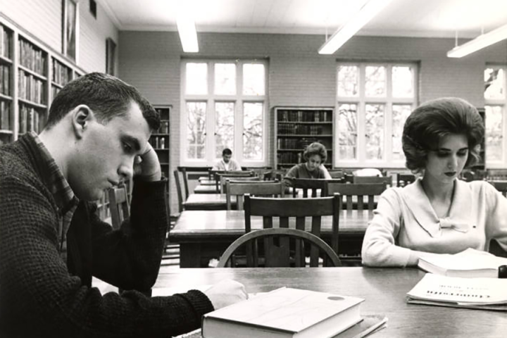 Black-and-white photograph of students studying inside of the Fletcher Hall library. 