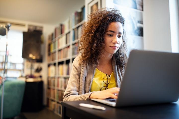 Woman with yellow shirt in library studying on laptop