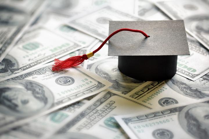 Graduation hat with red tassle with hundred dollar bills beneath. 