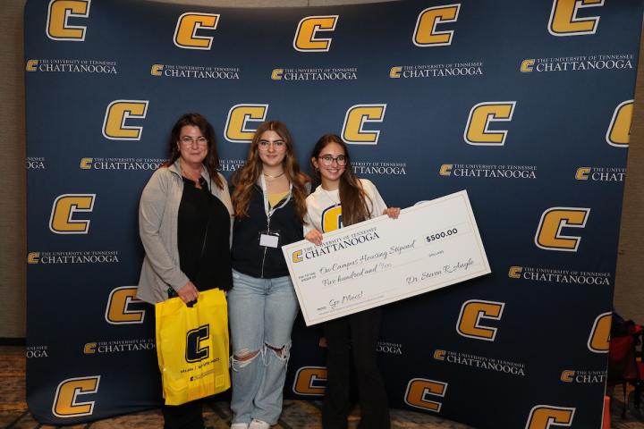 Future UTC students and parent standing with a large check in front of a Power C background