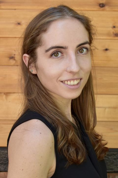 Woman with brown hair wearing a black shirt standing in front of a wooden backdrop.