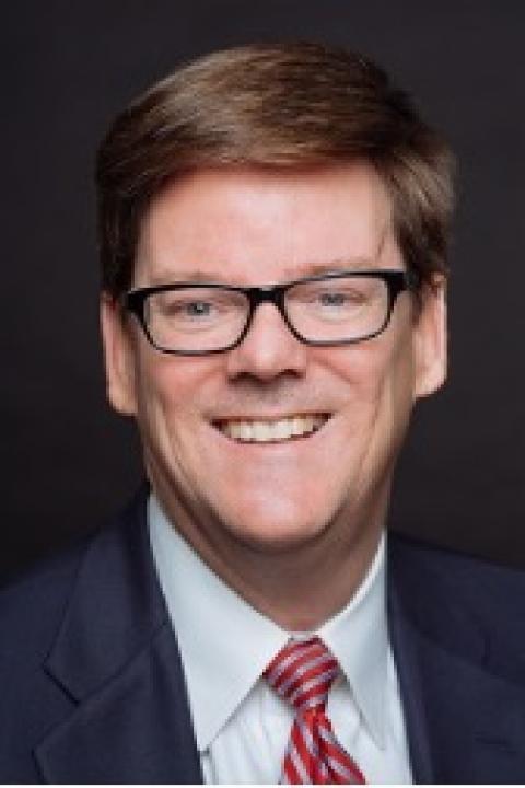 Headshot of David Higney in a dark suit, white shirt, and red tie. 