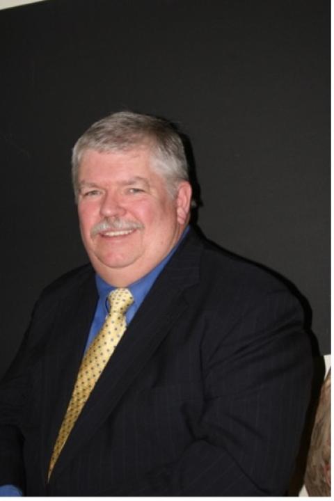 Headshot of Earl Brown in a black suit, blue button-down shirt, and yellow tie.