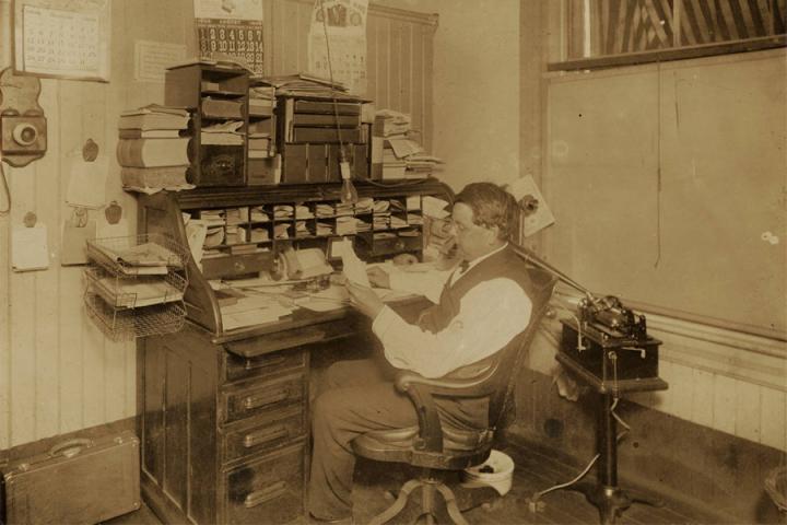 Black-and-white photograph of a Thatcher Medicine Company employee seated at a desk. 1909 or 1910