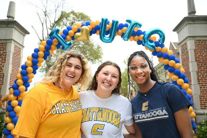 Three students standing under a balloon arch that reads "I Heart UTC"