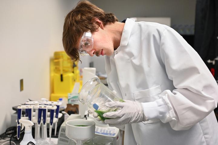 UTC student pouring green liquid from a glass container into a beaker