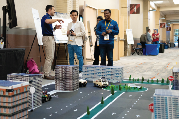 People standing behind a 1/10th scale roadway with remote controlled cars