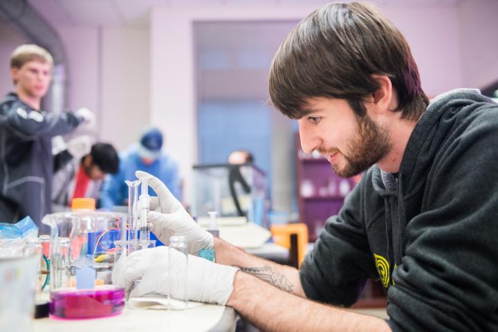 Male student in a lab using a syringe to draw up a liquid.