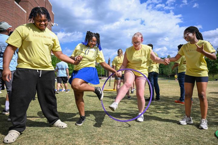 Students holding hands and stepping through a hula-hoop.
