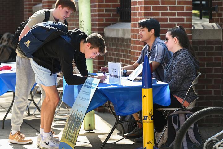 Students writing and talking with people sitting at a table booth.