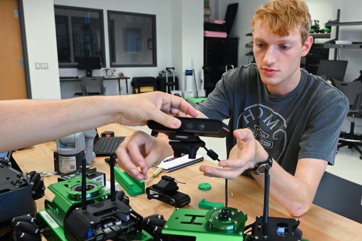 Someone handing a student a piece for small robot being made.