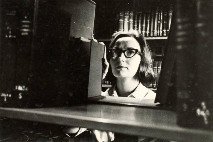 Black-and-white photograph of a student looking at books in the Fletcher Hall library. This photograph is undated.