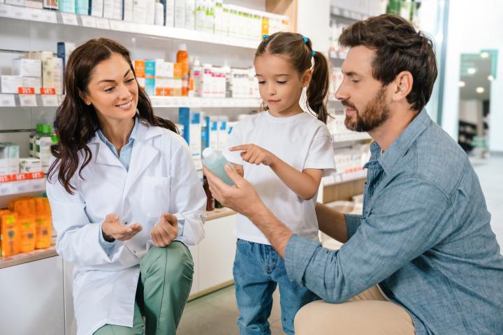A female pharmacy technician helps a single dad with his young daughter's medication