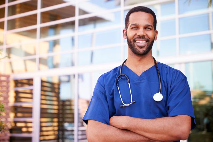 Male CNA standing and smiling outside of the hospital
