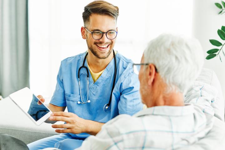 A male CNA supports his elderly patient at home
