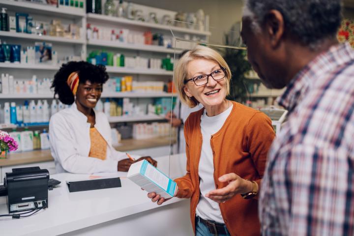 A female pharmacy technician helps an older couple with their medicine