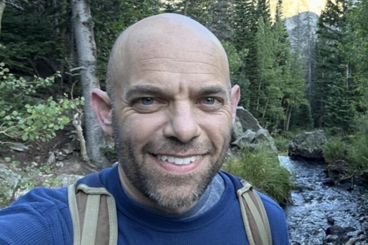 Dean Bingham hiking with mountain and a stream in the background.