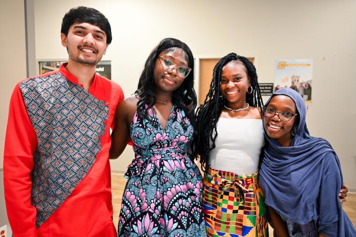 Four students in traditional and cultural attire smile together at International Student Week Kickoff.