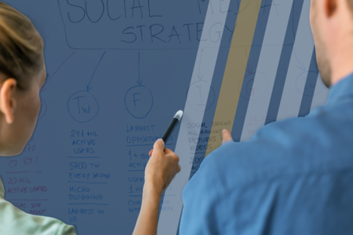 A woman shows points to a whiteboard that shows a "social strategy" while a man listens.