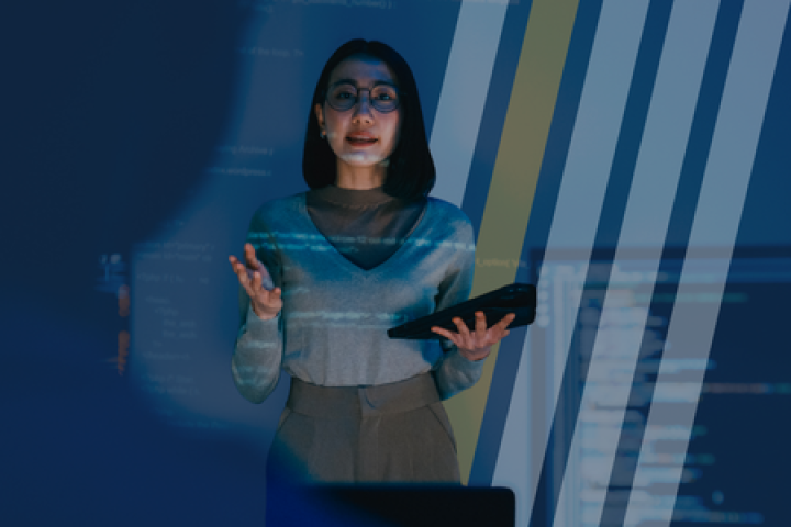 A woman stands in front of a room presenting data to co-workers. 