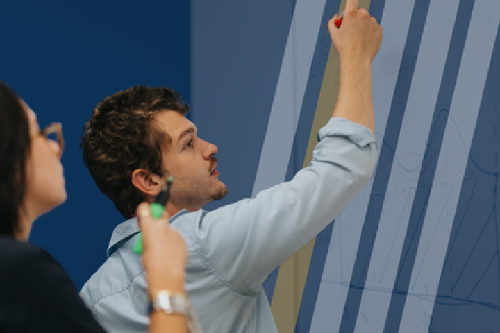 Two students write work on a classroom assignment on a whiteboard.