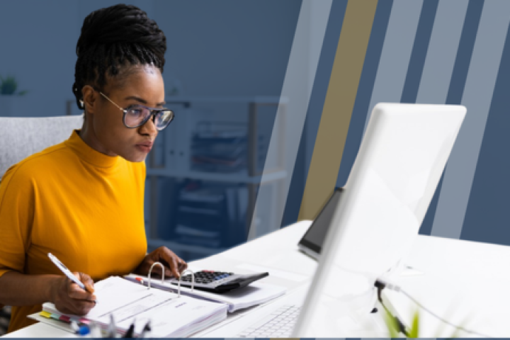 Woman sits in front of a computer and calculator taking notes.
