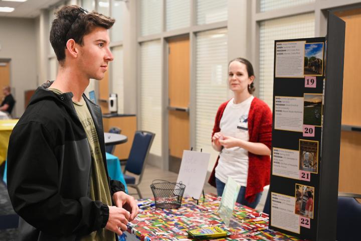Student talking with staff at a Study Abroad Fair table with a program display board.