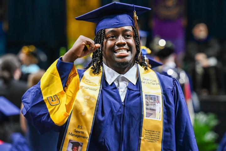 Graduate in navy graduation gown and gold sash