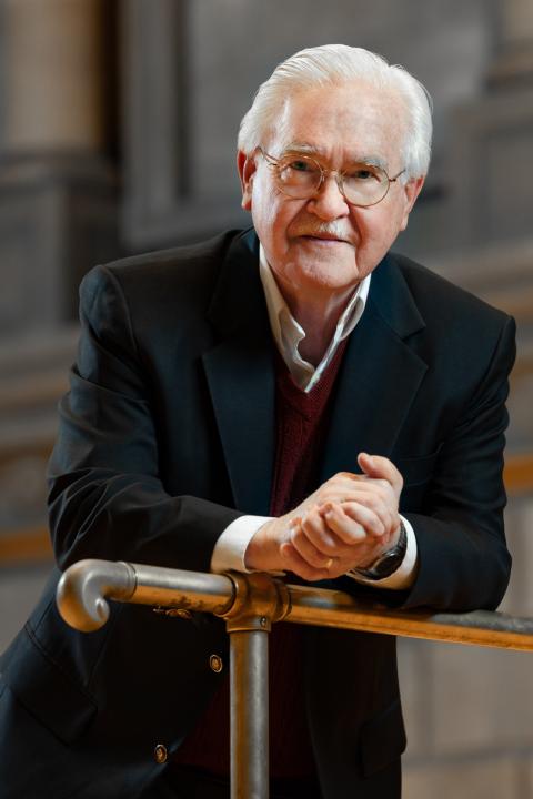 Elderly man leaning on podium in suit.