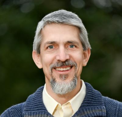 Middle-aged, well-groomed man with facial hair and warm smile.