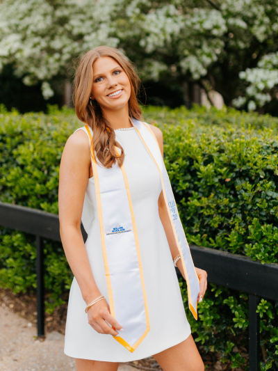 Alyson posing in front of a bush with her graduation stole.