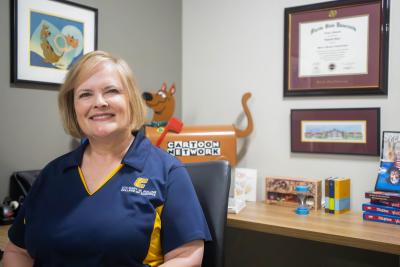 Professor Libby Fakier sits at her desk in her office surrounded by souvenirs from her past work with cartoon network. 