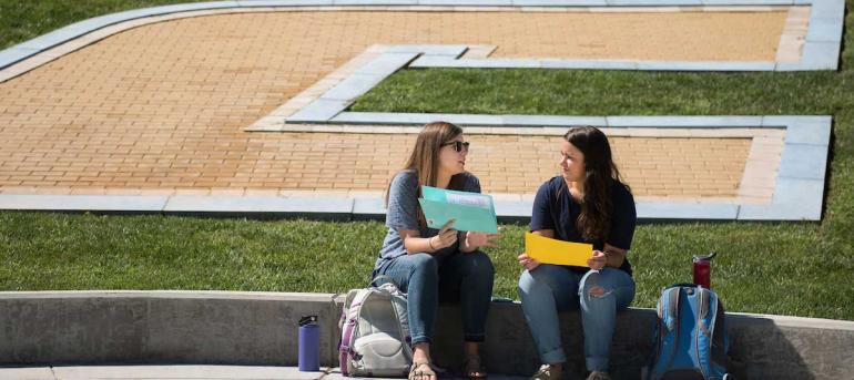 two students sitting in front of the UTC logo on chamberlain field