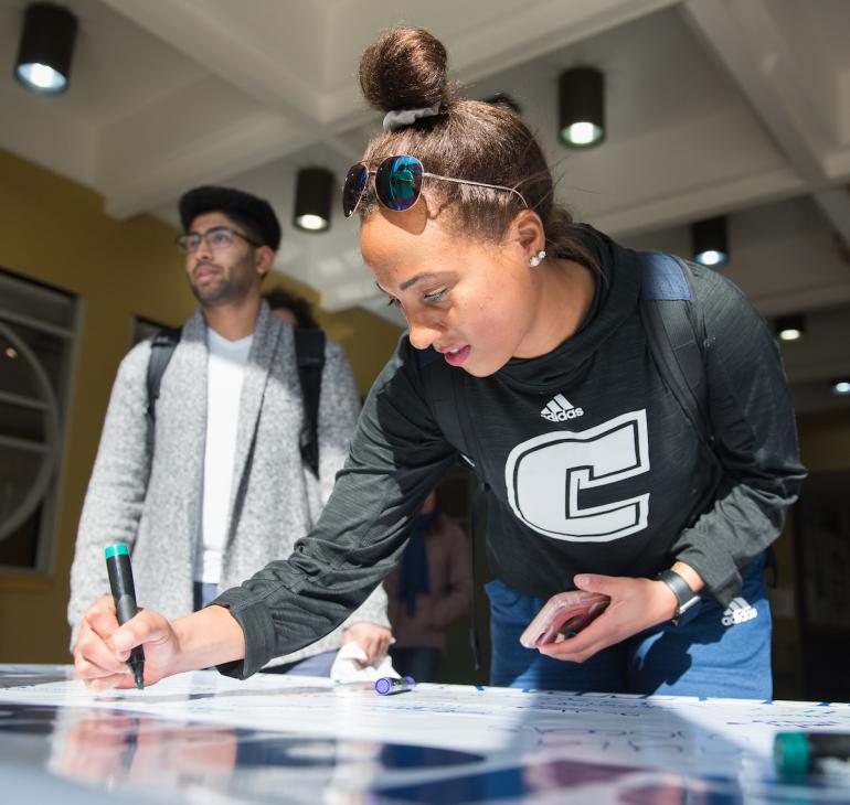 two students of color, one signing a poster board, the other waiting to sign. two students of color, one signing a poster board, the other waiting to sign.