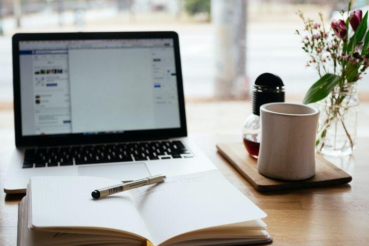 an open notebook in front of an open macbook with a coffee mug sitting to the right