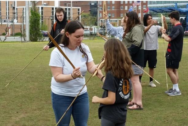 Young girl is shown how to use wooden bow