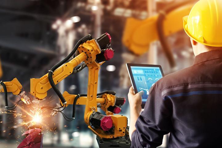 Man in hardhat using robotic machine in factory