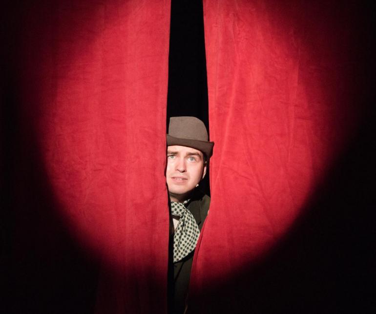 male cast member sticks head out between curtains