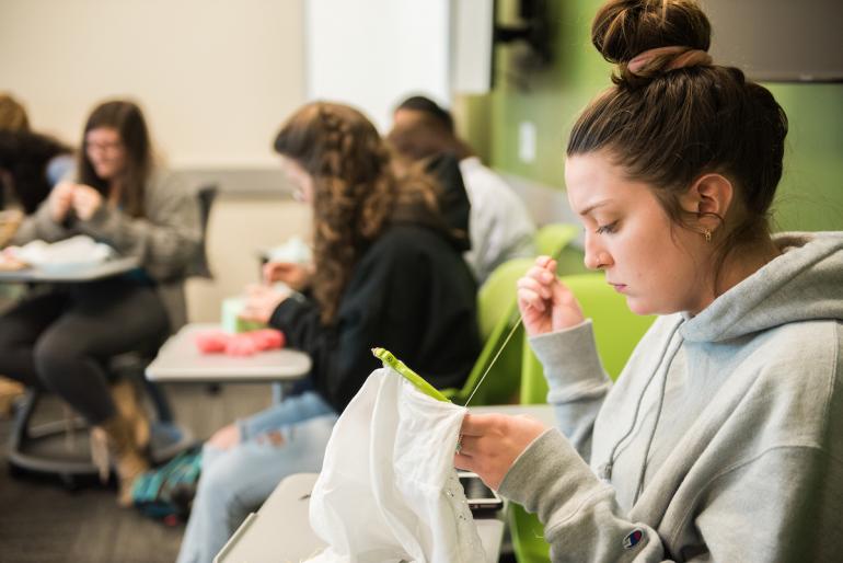 female student in women, gender, and sexuality class class cross stitching